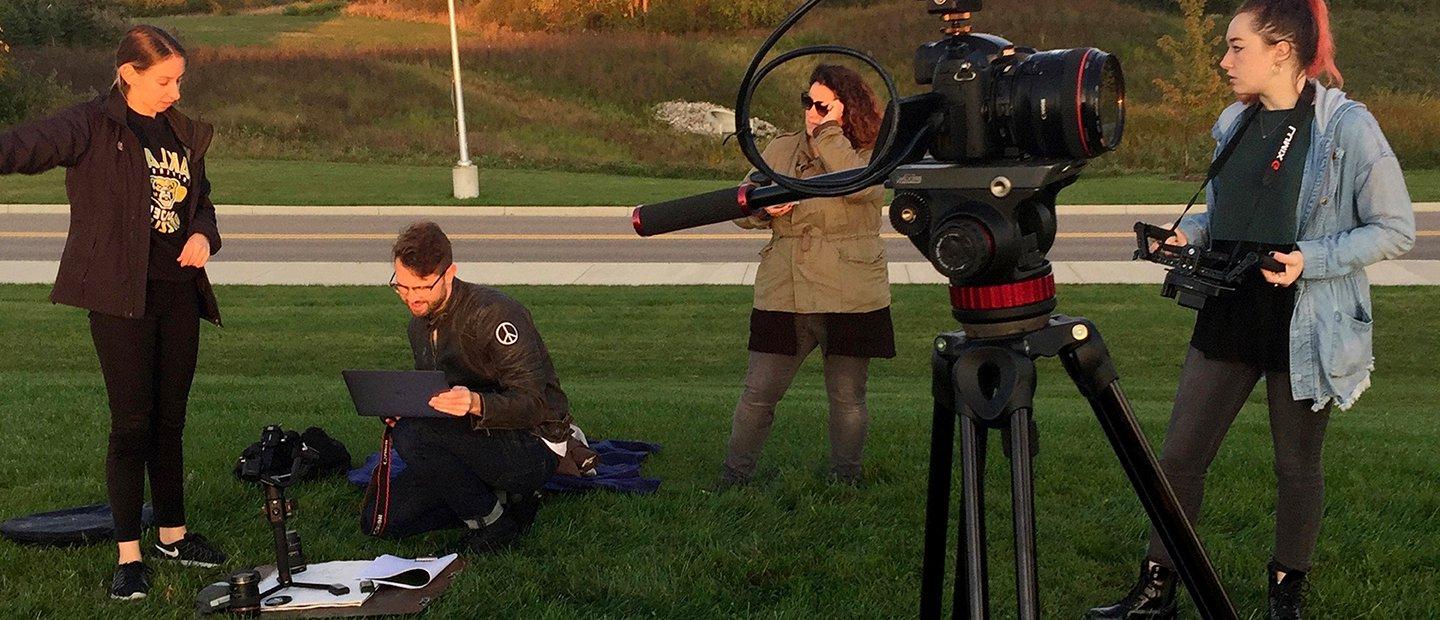 A team of four people shooting and reviewing video outdoors.